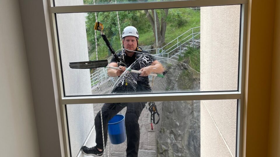 Daniel Hackett utför fönsterputs med repteknik vid hög byggnad. 