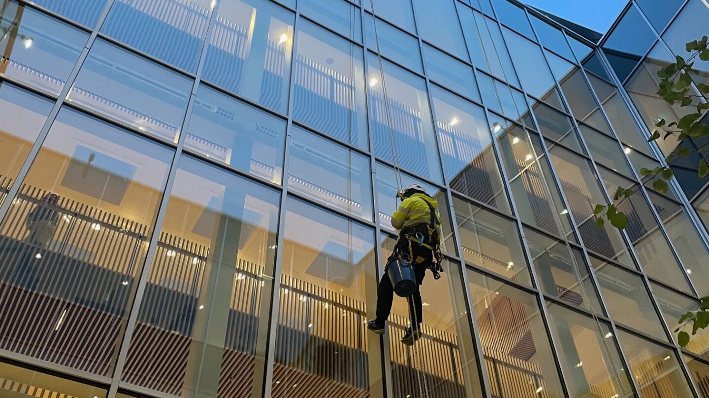 Daniel Hackett utför fönsterputs med repteknik vid en hög byggnad.